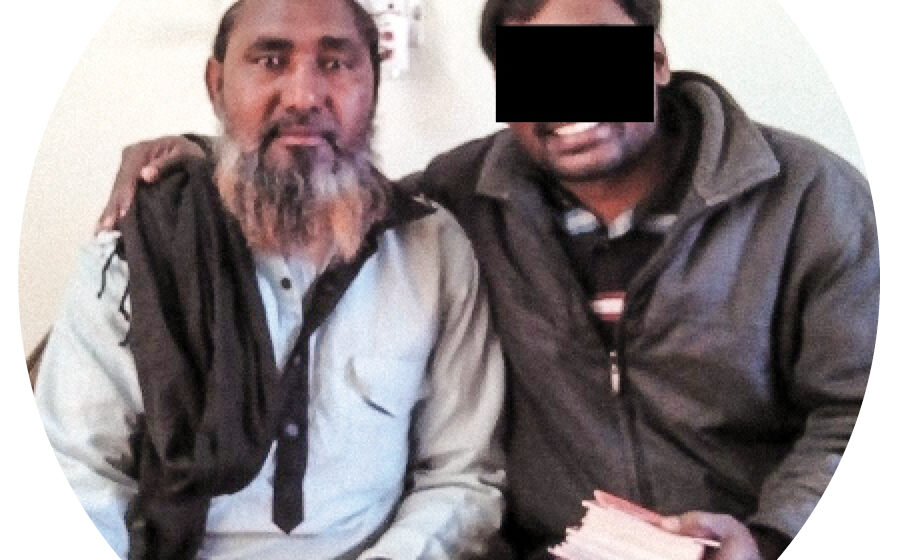Two men sitting together smiling and one has a black box over his eyes and is holding a bible